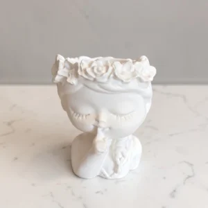Figurine décorative Secret Fleuri représentant un visage féminin aux yeux fermés, avec une couronne de roses et un doigt posé sur les lèvres.