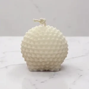 Bougie décorative sphérique rose avec reliefs ondulés et mèche en coton nouée, photographiée sur un fond en marbre blanc.